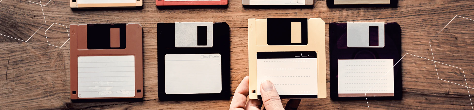 a row of four floppy disks. the third is being picked up by a human hand.